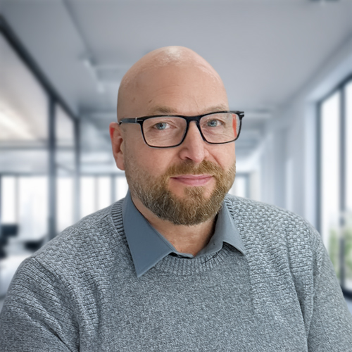 Mann mit Glatze, Brille und grauem Pullover in einem hellen Büro.